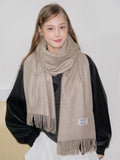 Woman wearing a beige scarf with fringe detail around her neck.