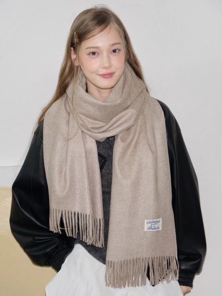 Woman wearing a beige scarf with fringe detail around her neck.