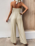 Back view of a woman in a cream sleeveless jumpsuit with a smocked back and wide legs.
