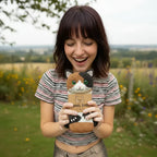 A smiling woman holding a calico cat novelty sock in an outdoor setting.