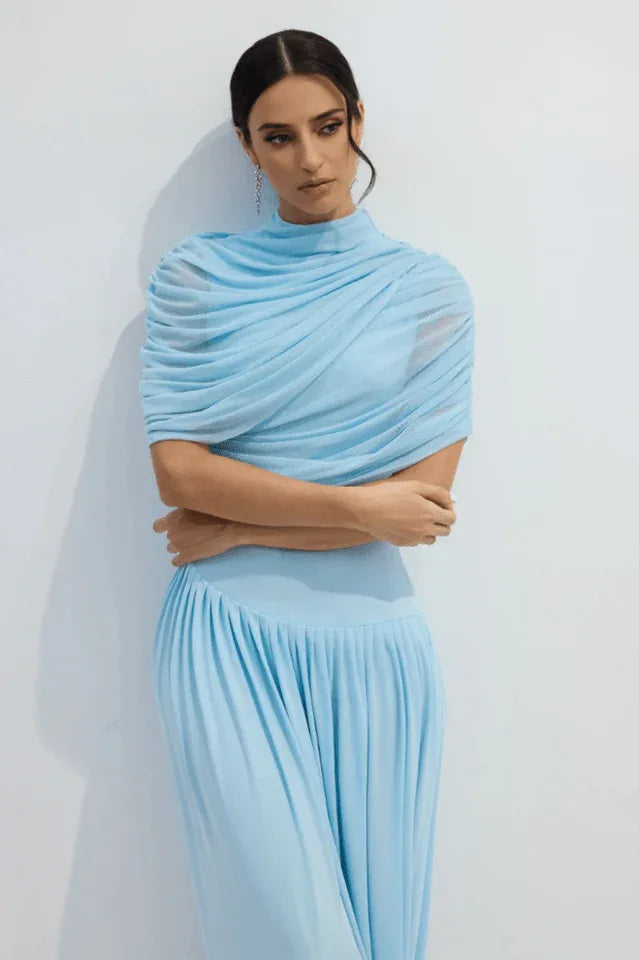 Close-up of a woman's upper body in a light blue draped jersey dress, showing the ruched neckline.