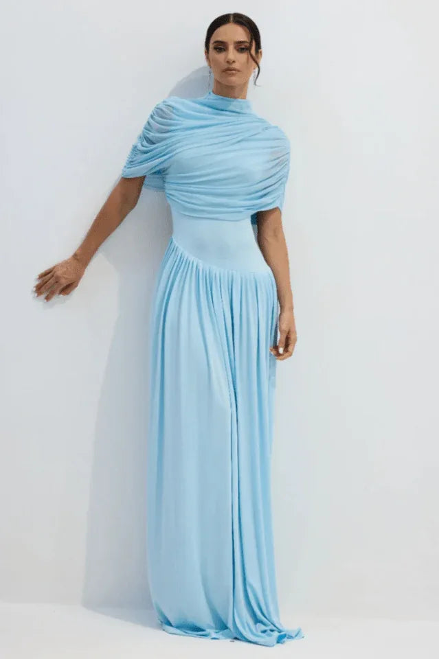 Woman wearing a light blue draped jersey maxi dress with a high neckline and pleated skirt.