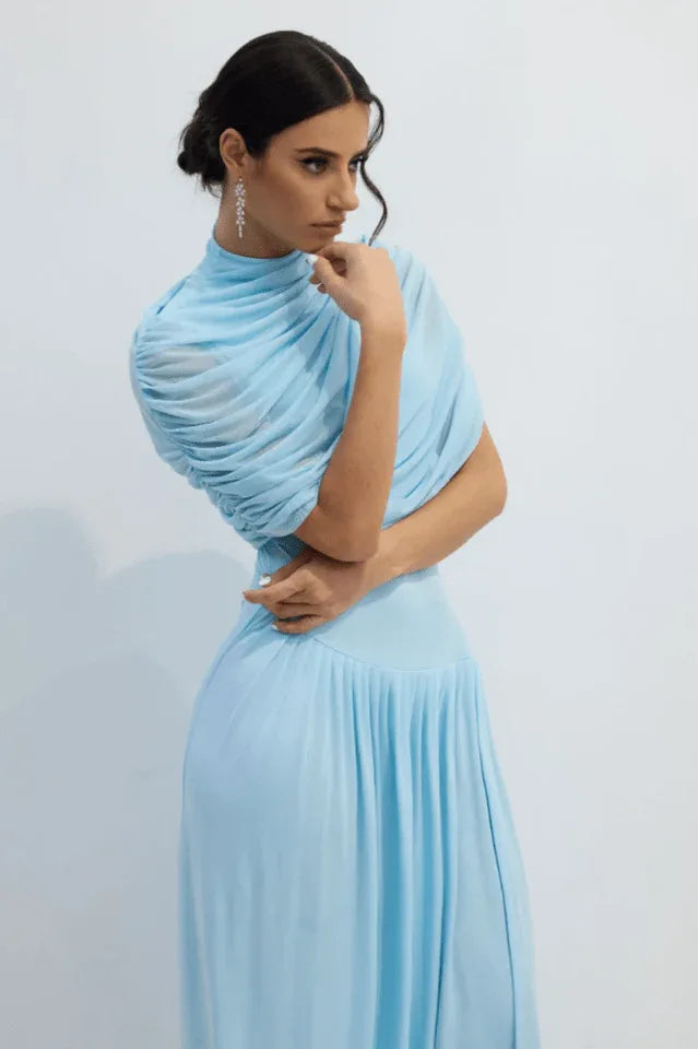 Woman posing in a light blue draped jersey maxi dress with a turtleneck and pleated skirt.