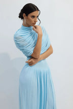 Woman posing in a light blue draped jersey maxi dress with a turtleneck and pleated skirt.