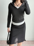 Full body shot of a woman wearing a charcoal grey hooded zip-up top, white tank, and black skirt, accessorized with a necklace and handbag.
