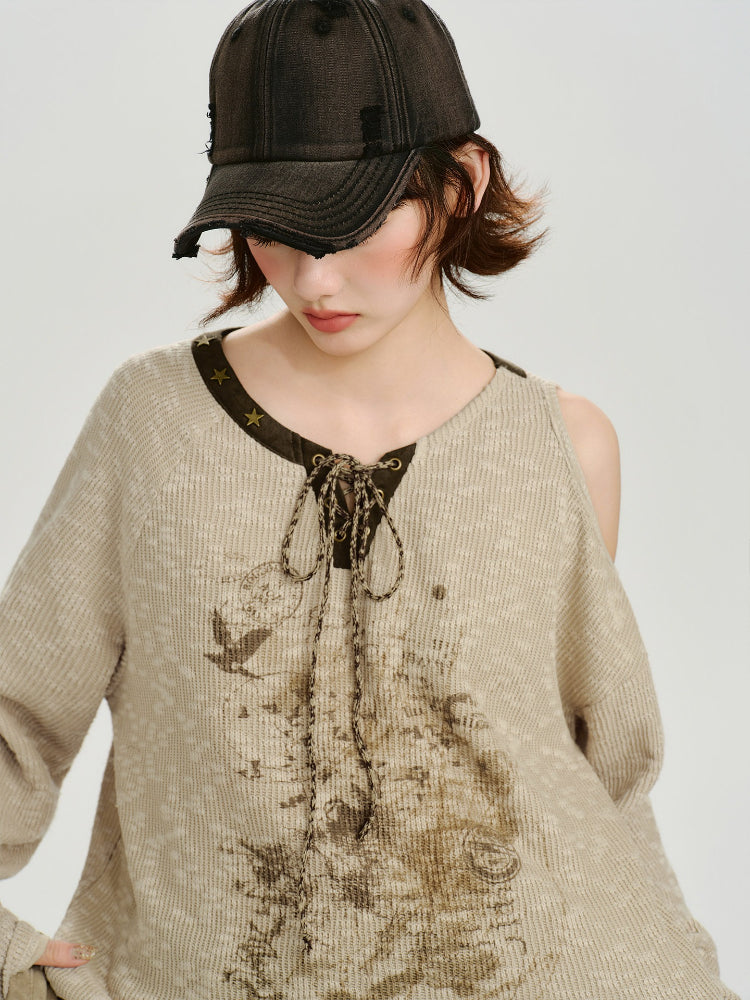 Front view of a woman in a beige knit sweater with a graphic print and cold shoulder design.
