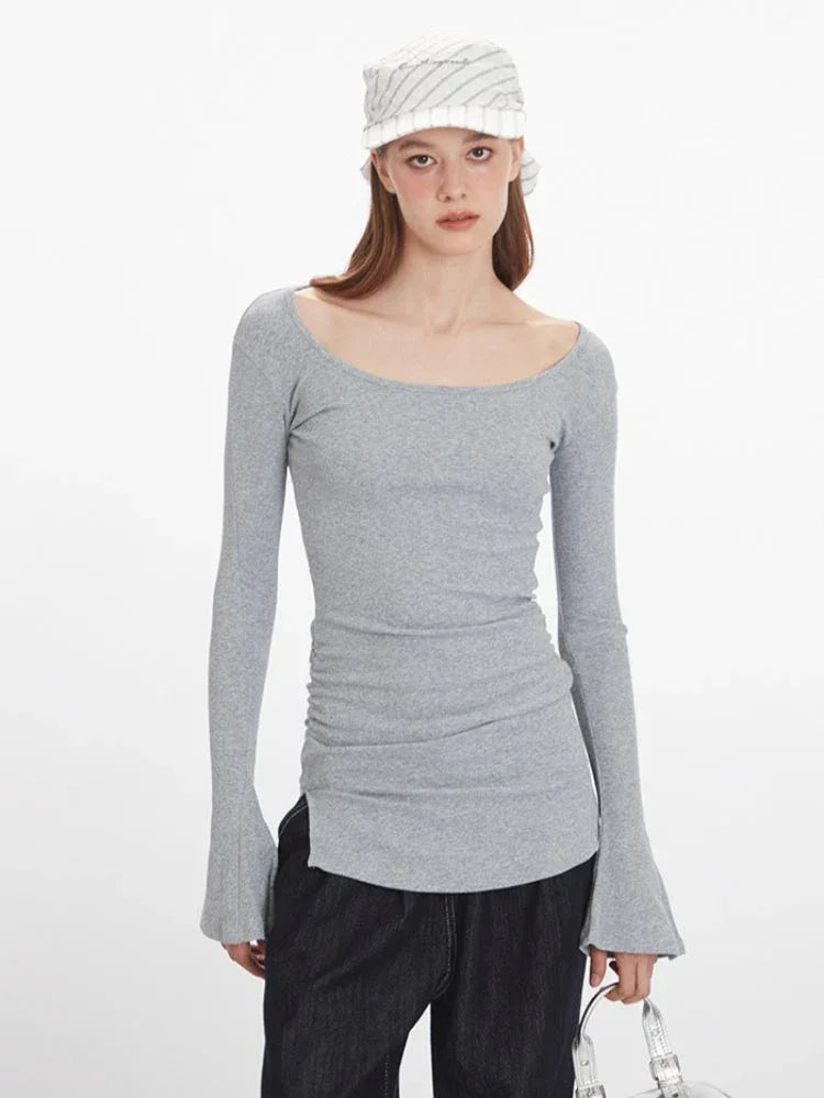 Front view of a woman wearing a grey long-sleeved ribbed knit top with a scoop neckline, ruched side detail, flared cuffs, and a side slit hem.