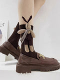 Close-up of brown crew socks with a 3D bunny embellishment and striped scarf detail.