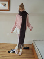 Woman in a pink cardigan and scarf, posing with one leg bent.