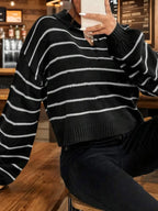 Woman holding a white phone while wearing a black and white striped cropped knit sweater.