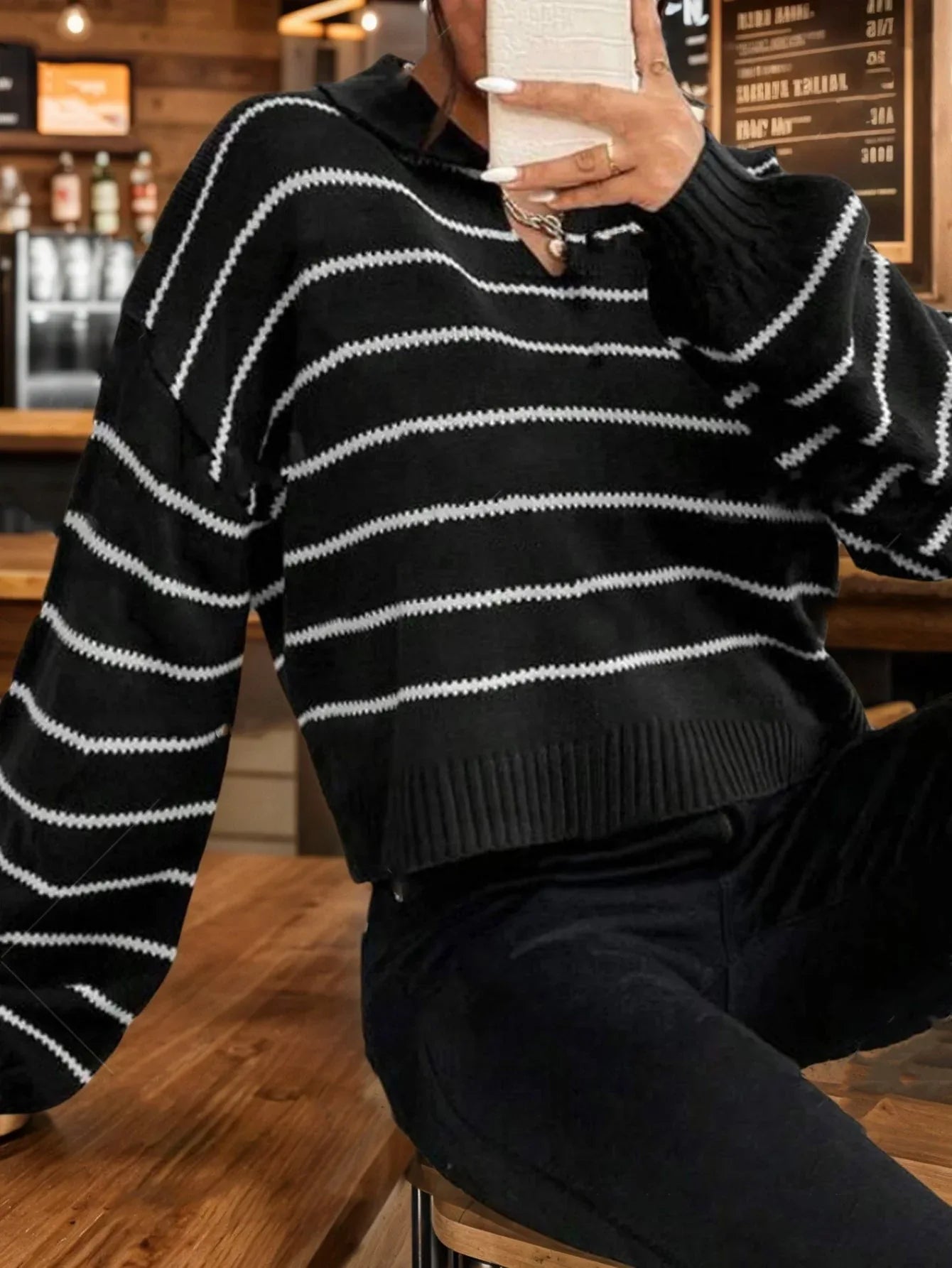 Woman holding a white phone while wearing a black and white striped cropped knit sweater.
