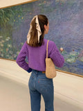 Woman from behind wearing a purple cable knit cardigan and blue jeans.