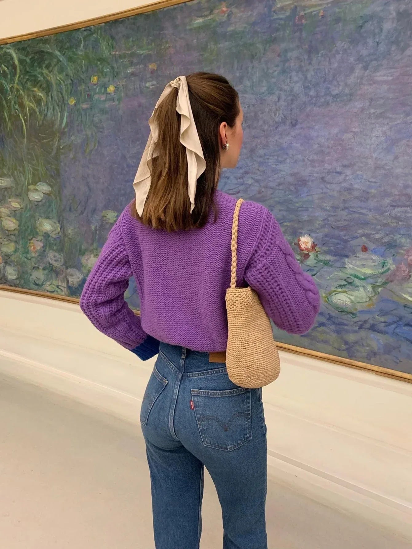 Woman from behind wearing a purple cable knit cardigan and blue jeans.