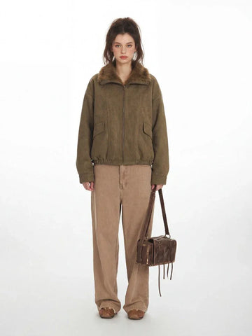 Woman wearing a green corduroy bomber jacket with a faux fur collar and tan wide-leg pants, holding a brown leather crossbody bag.