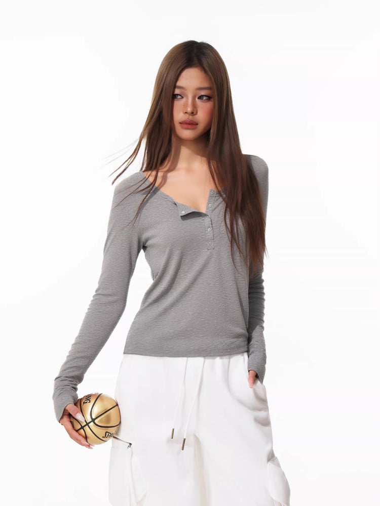 Woman wearing a grey long-sleeve henley shirt and white cargo pants, holding a mini basketball
