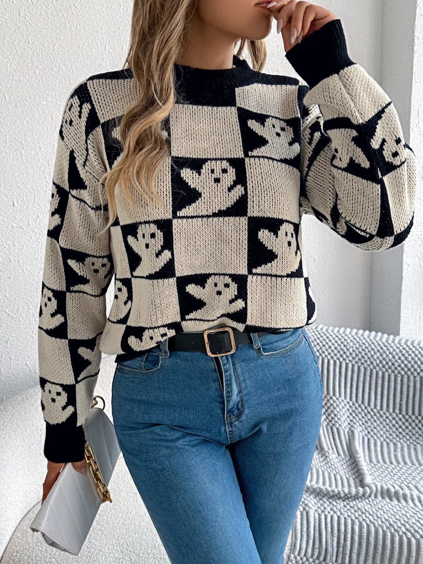 Woman adjusting her hair while wearing a black and cream checkerboard knit sweater with ghost print and blue jeans.