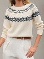 Woman wearing a cream-colored knit sweater with a black and grey Fair Isle pattern, paired with white pants and a brown belt.