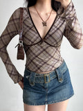 Woman wearing a brown plaid long-sleeve top with a V-neck and fitted silhouette.