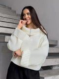 Woman smiling and touching her face while wearing a white knit cropped sweater with a half-zip closure.