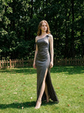 Woman in a grey one-shoulder satin gown standing in a grassy area with trees