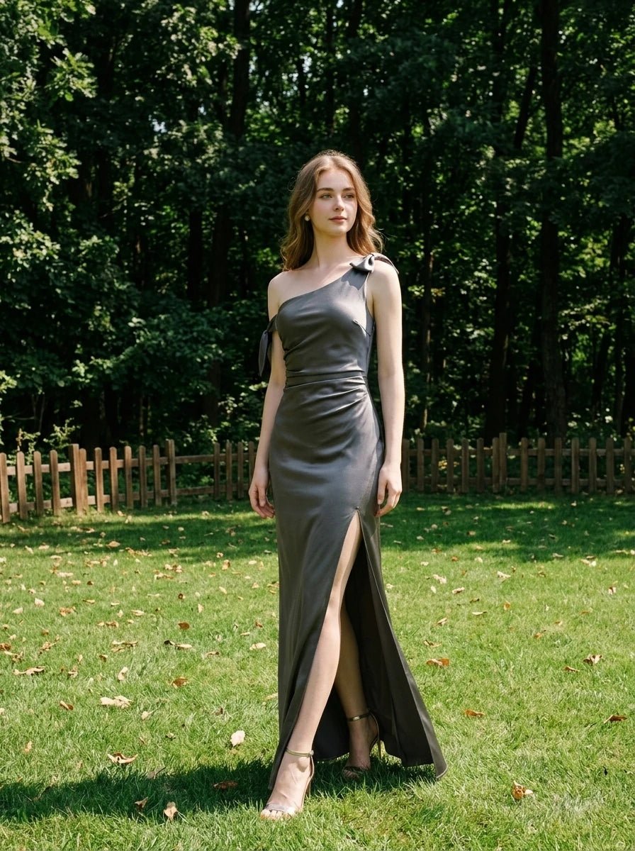 Woman in a grey one-shoulder satin gown standing in a grassy area with trees