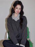 Woman sitting on a chair wearing a grey V-neck sweater and checkered shirt