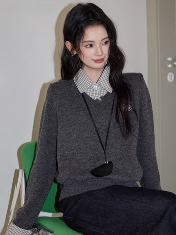 Woman wearing a grey V-neck sweater over a checkered collared shirt
