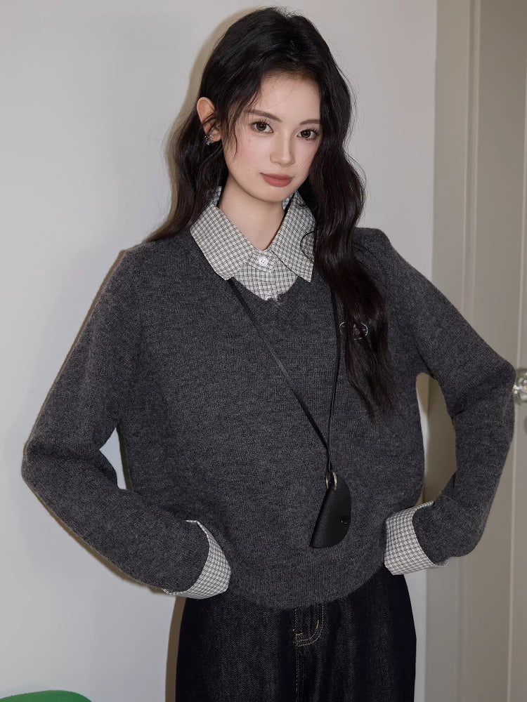 Woman with hands on hips wearing a grey V-neck sweater and checkered shirt