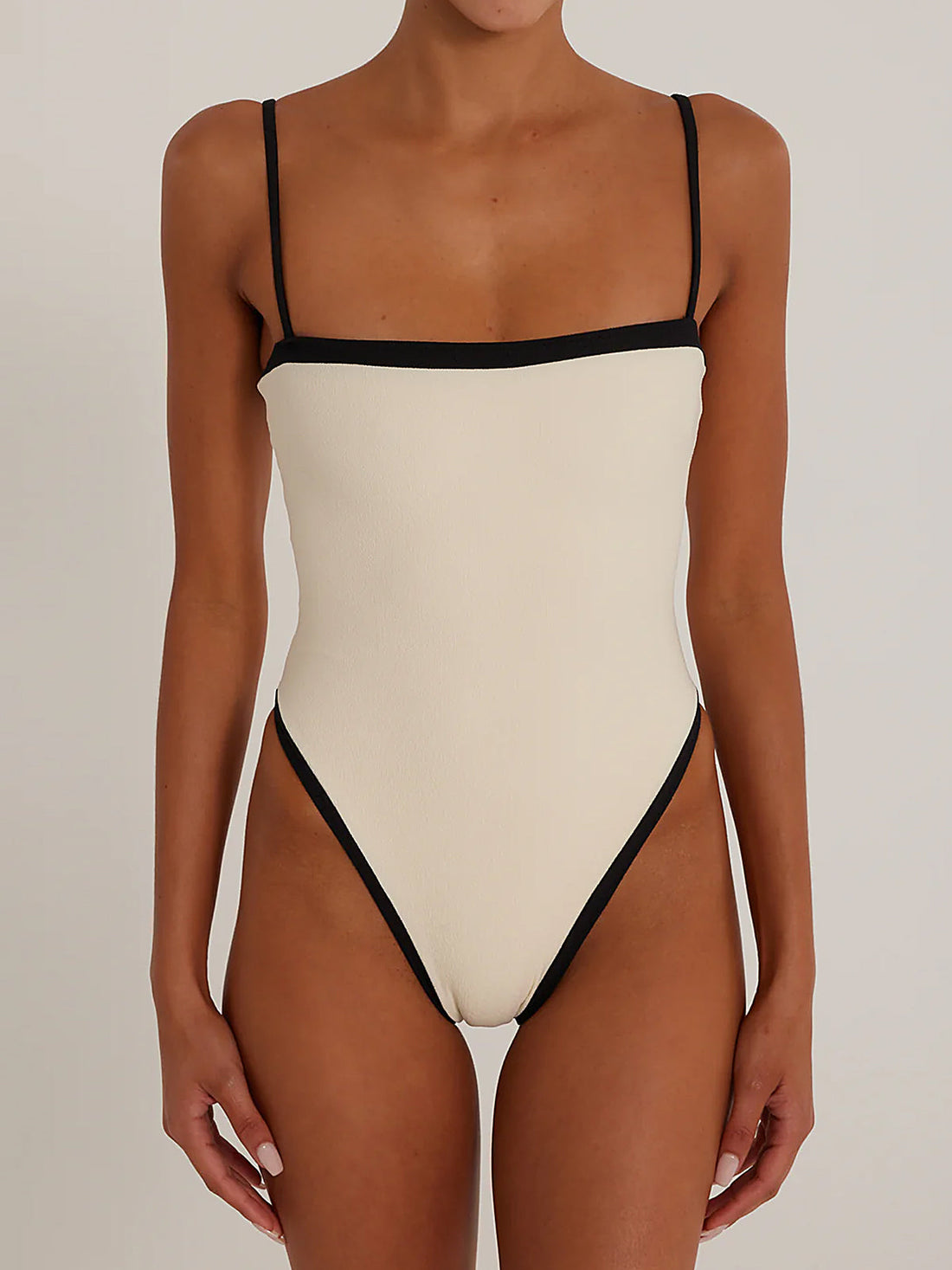 Woman wearing a black one-piece swimsuit with white trim and spaghetti straps.