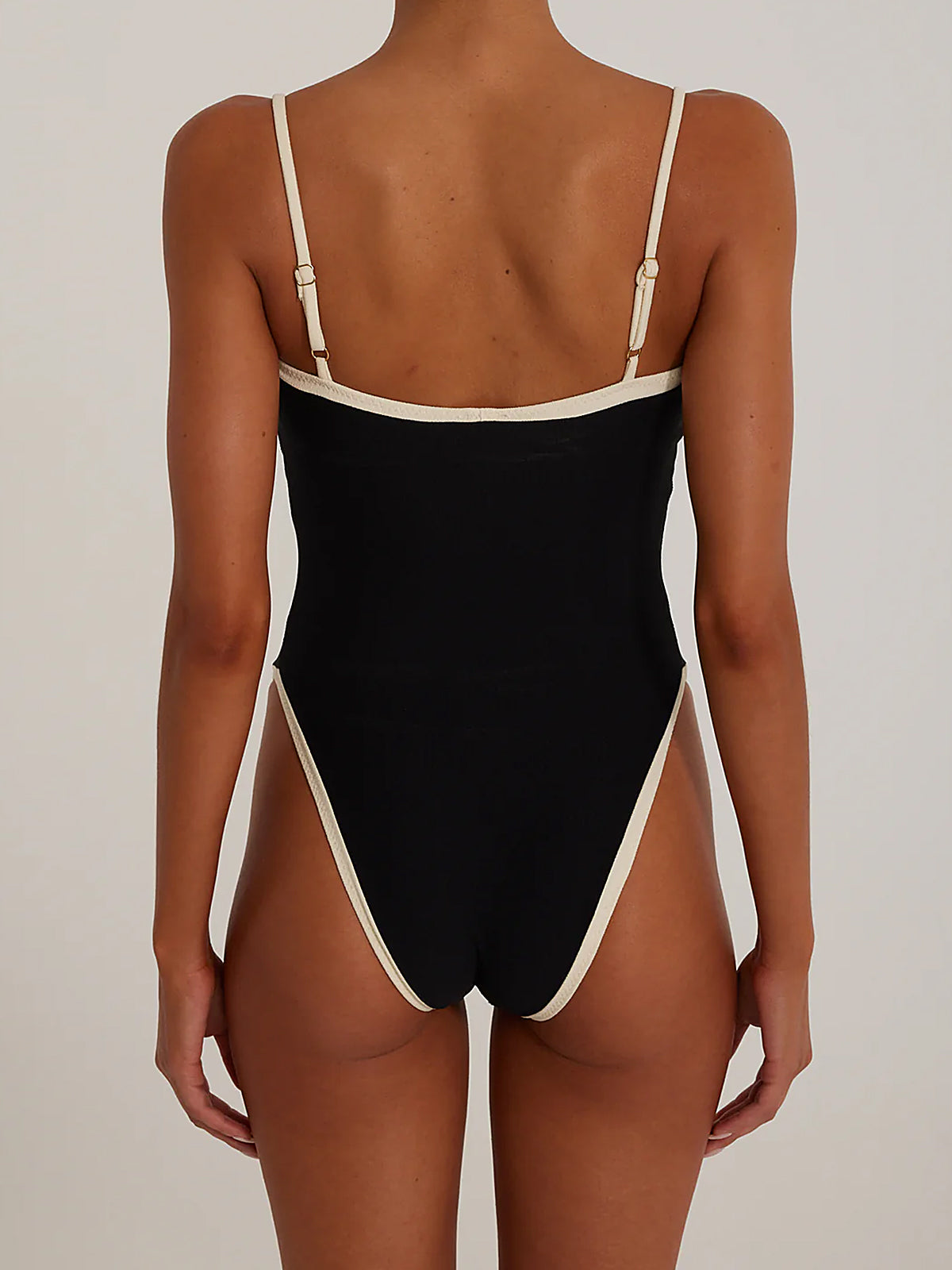 Back view of a woman in a black one-piece swimsuit with white trim.