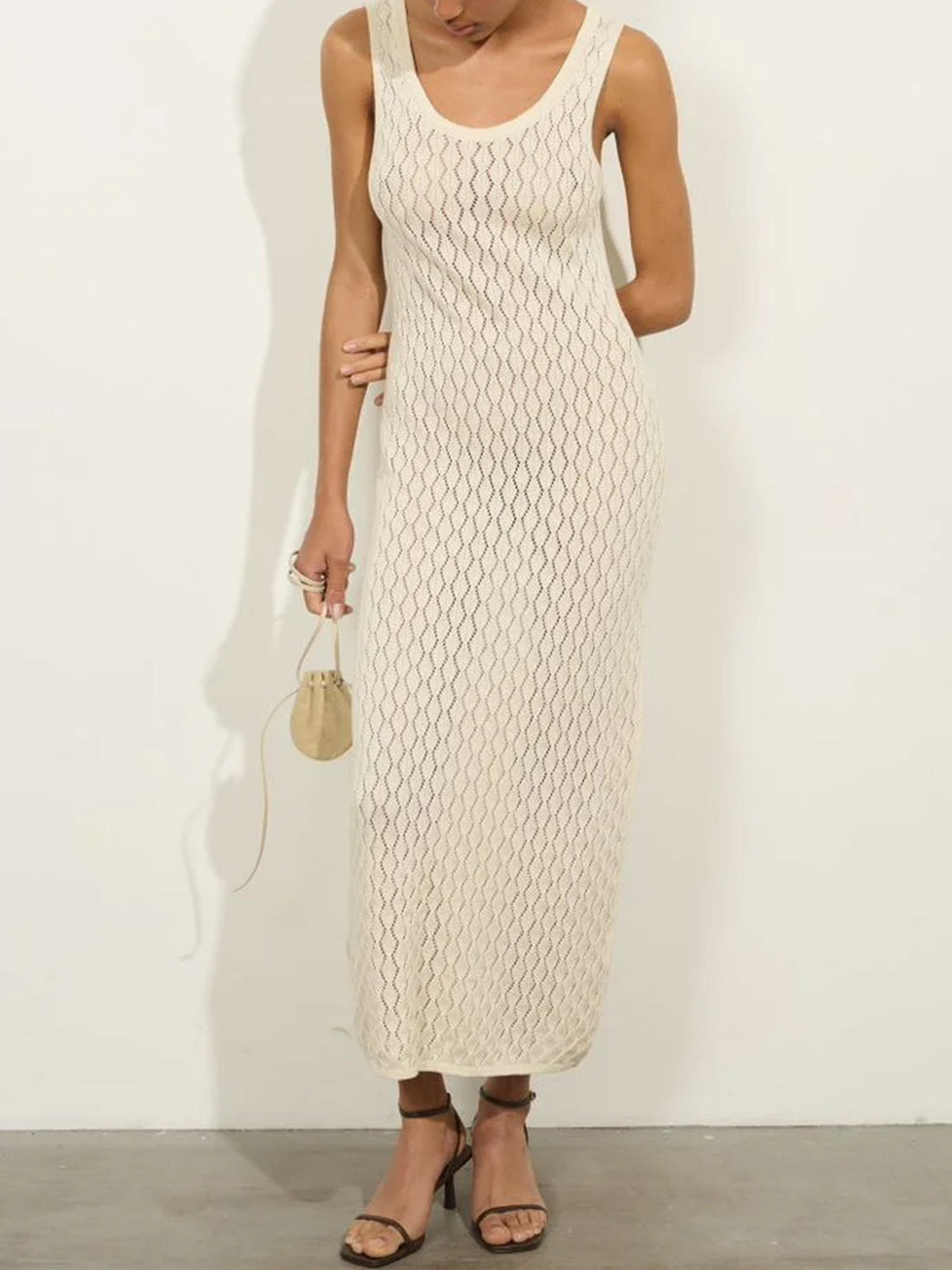 woman wearing a pale yellow sleeveless maxi dress with a scoop neck and textured knit pattern, holding a small beige handbag