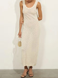 woman wearing an off-white sleeveless maxi dress with a scoop neck and textured knit pattern, holding a small beige drawstring pouch bag
