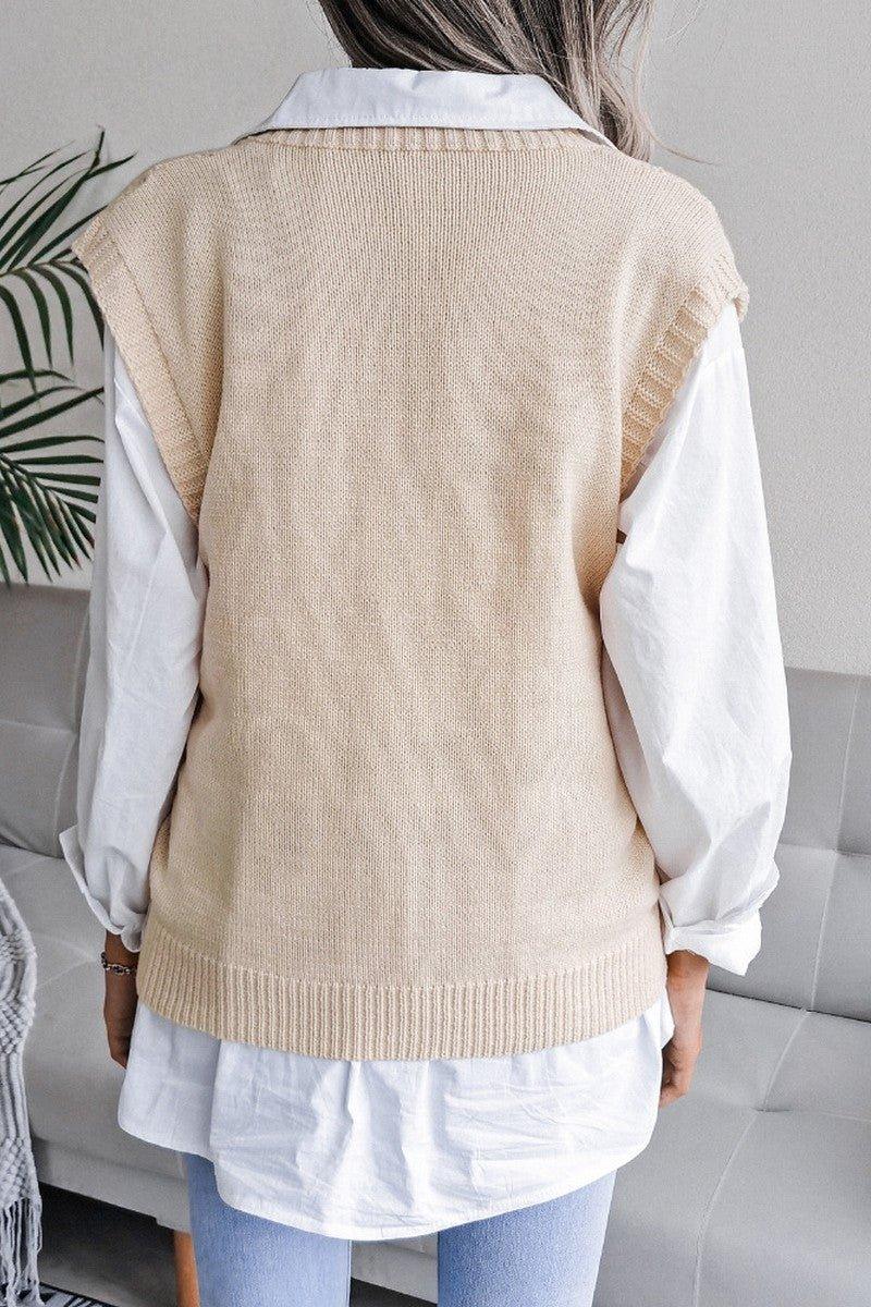 Back view of a woman wearing a beige cable knit V-neck sleeveless sweater vest over a white collared shirt.