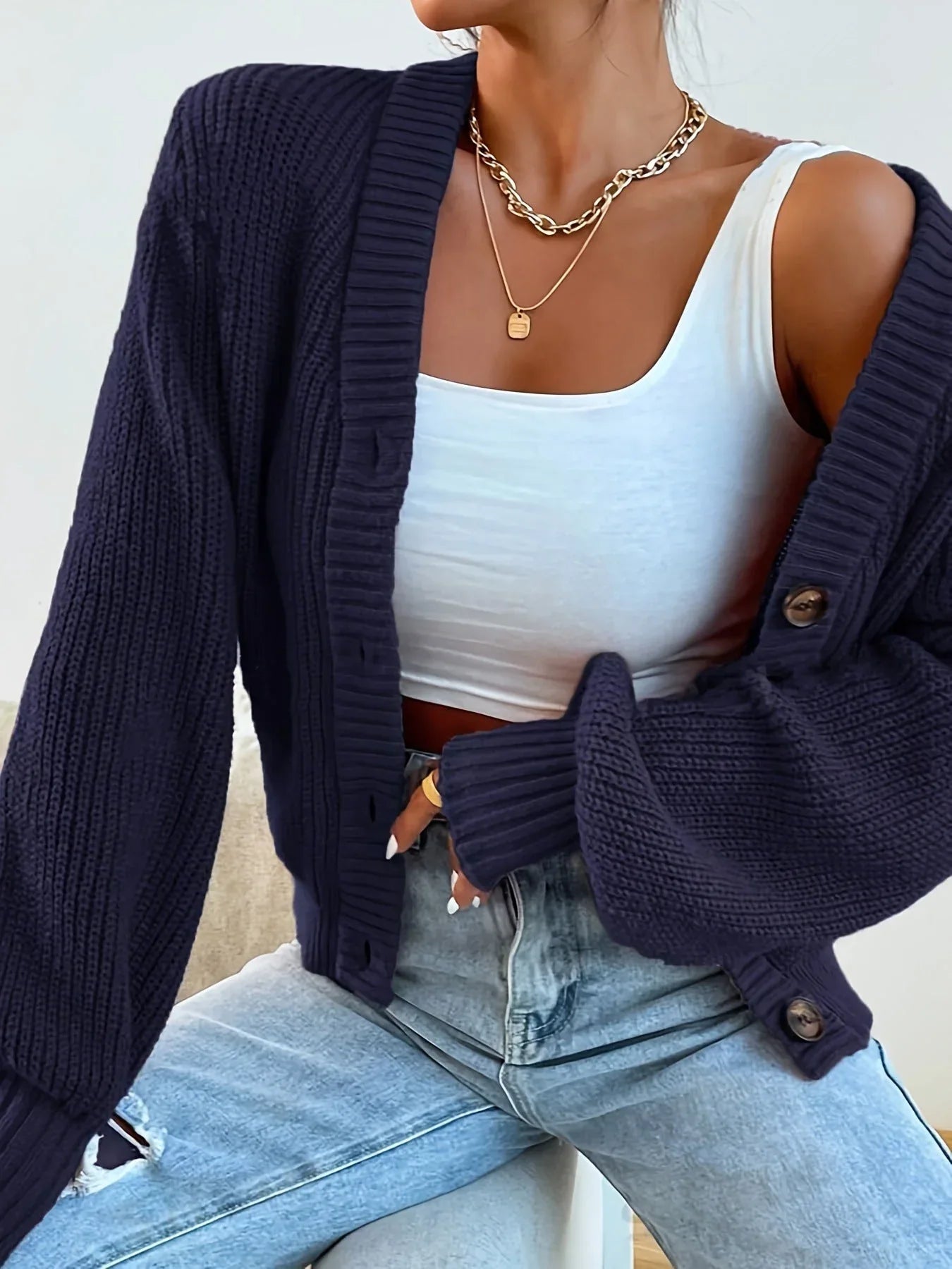 woman wearing a dark blue knit cardigan with a v-neck and button front, paired with ripped jeans
