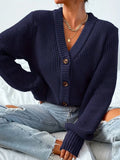 woman wearing a dark blue knit cardigan off the shoulder, holding a white handbag
