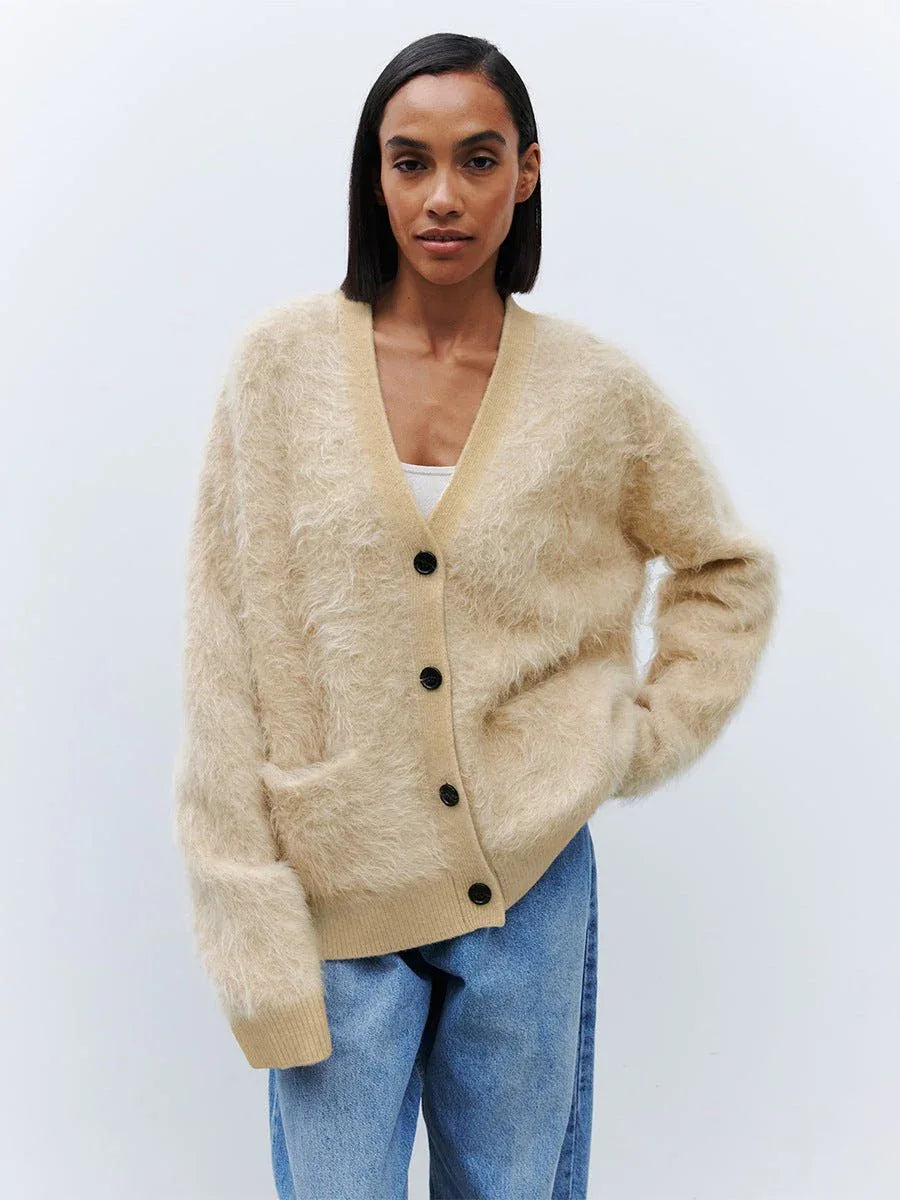Woman wearing an oatmeal colored faux fur button cardigan with a V-neckline and front pockets.