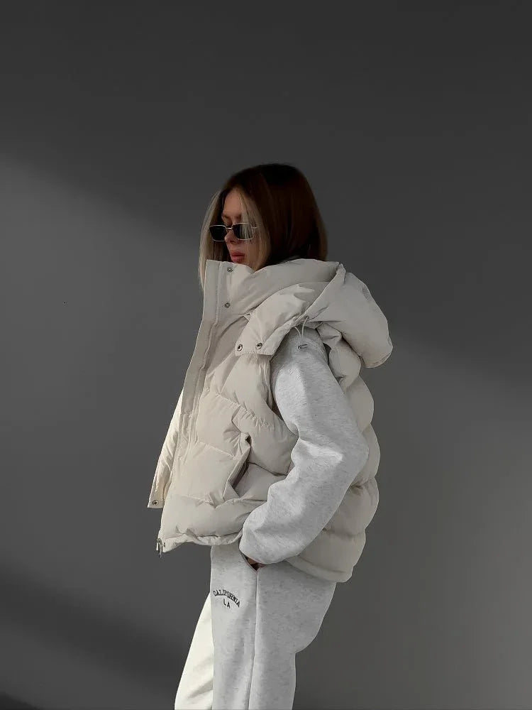 Woman with sunglasses wearing a cream puffer vest over a grey quarter-zip sweatshirt and sweatpants.