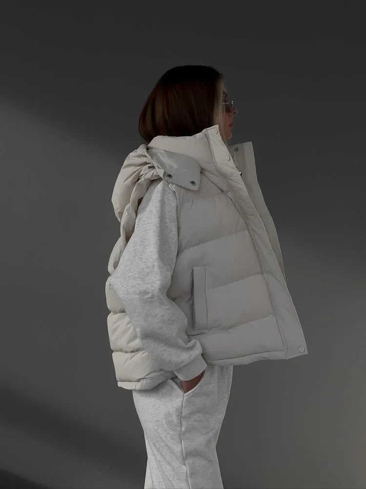 Side view of a woman in a cream puffer vest, grey sweatshirt, and sweatpants.