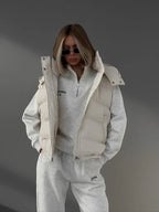 Woman wearing a cream puffer vest over a grey quarter-zip sweatshirt and sweatpants.