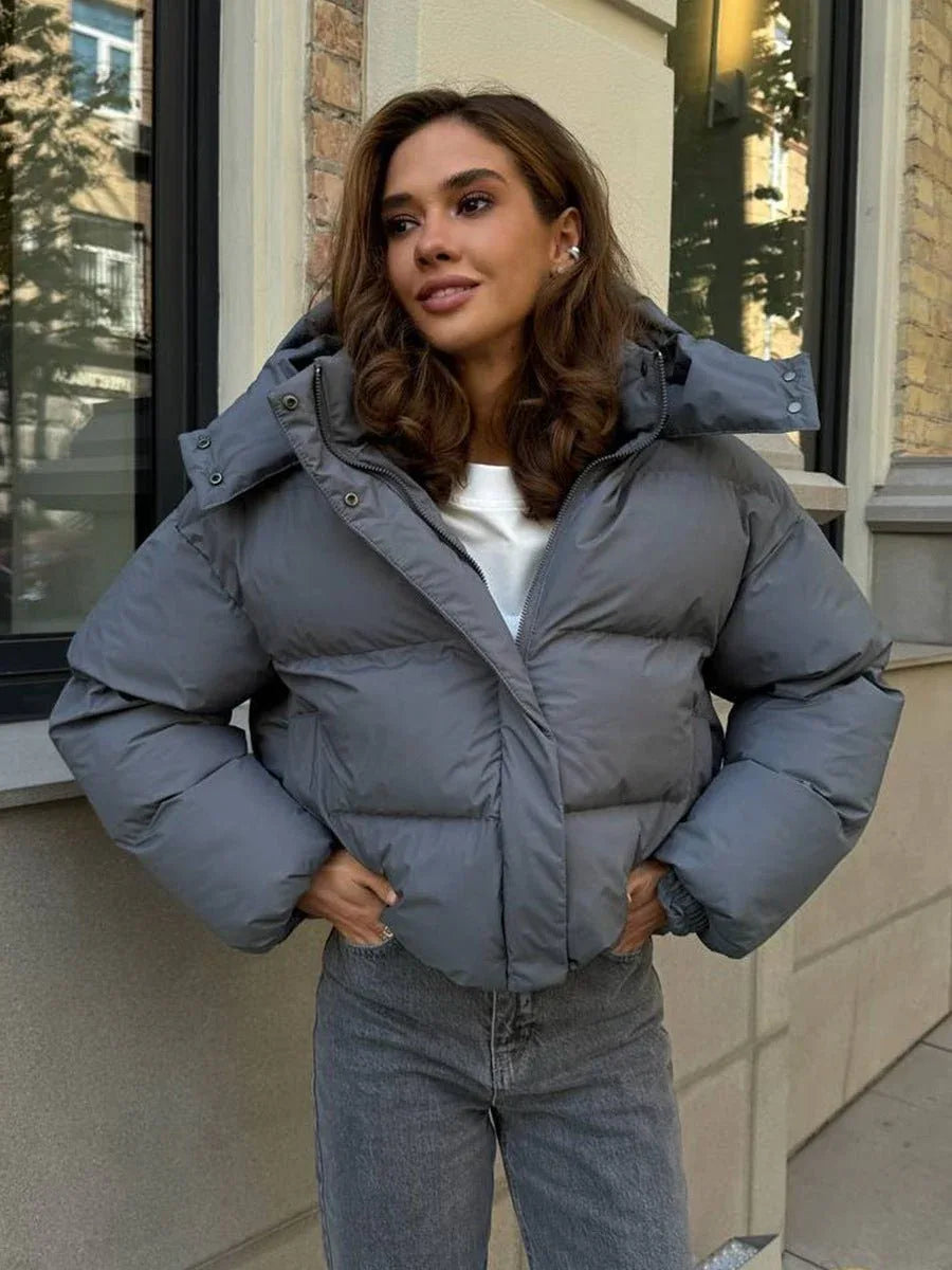 Woman wearing a grey hooded puffer jacket with a white t-shirt and grey jeans.