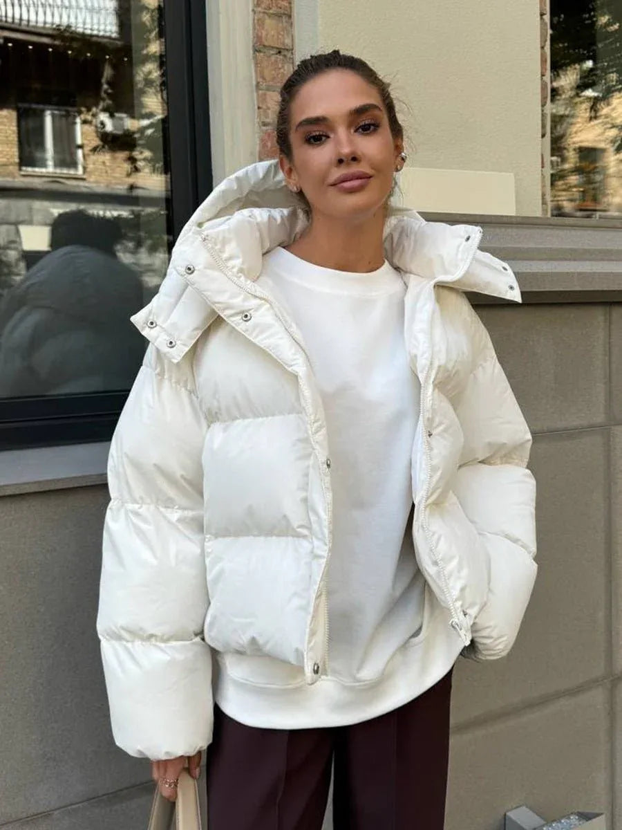 Woman wearing a white hooded puffer jacket with a white t-shirt and brown pants.