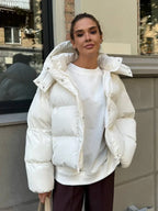 Woman wearing a white hooded puffer jacket with a white t-shirt and brown pants.