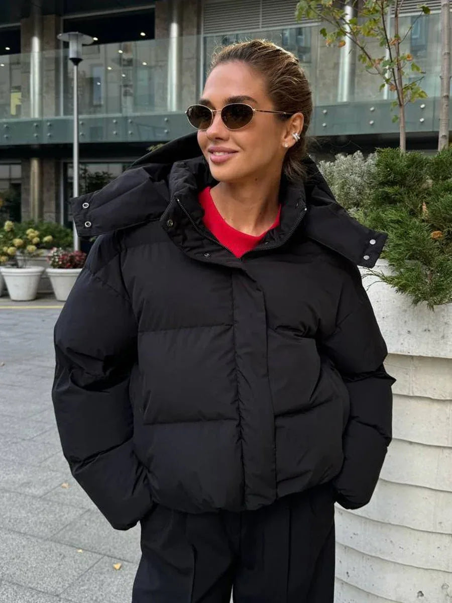 Woman wearing a black hooded puffer jacket with a red t-shirt and black pants.