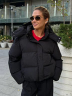 Woman wearing a black hooded puffer jacket with a red t-shirt and black pants.