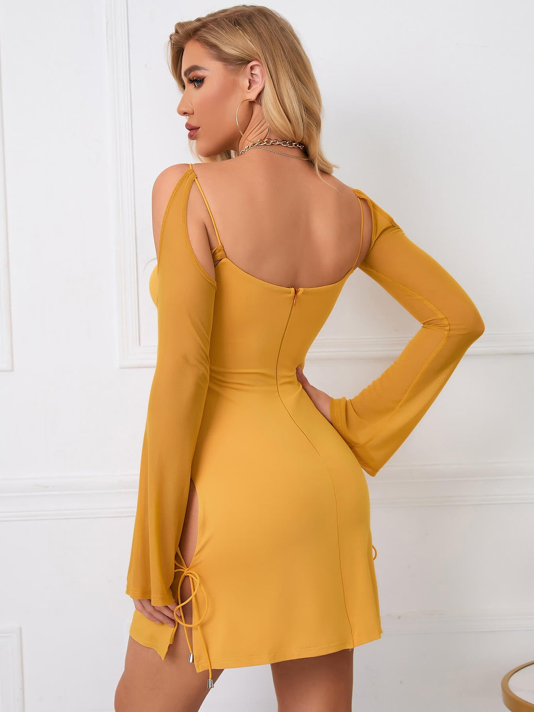Woman wearing a yellow bodycon dress with cutout details and long sheer sleeves.