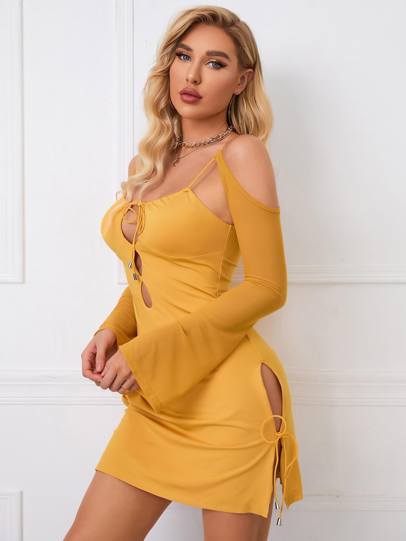 Front view of a woman in a yellow bodycon dress with cutout details and long sheer sleeves.
