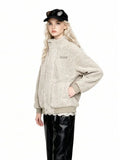 Three-quarter view of a woman wearing a beige sherpa fleece bomber jacket with a high collar, ribbed cuffs and hem, and an embroidered logo. She is wearing black leather pants and a black baseball cap with sunglasses.