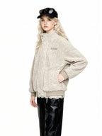 Three-quarter view of a woman wearing a beige sherpa fleece bomber jacket with a high collar, ribbed cuffs and hem, and an embroidered logo. She is wearing black leather pants and a black baseball cap with sunglasses.