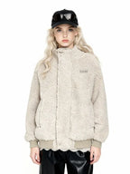 Front view of a woman wearing a beige sherpa fleece bomber jacket with a high collar, ribbed cuffs and hem, and an embroidered logo. She is wearing black leather pants and a black baseball cap with sunglasses.