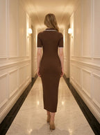 Back view of a woman wearing a brown ribbed knit midi dress with white collar trim, walking in a hallway.